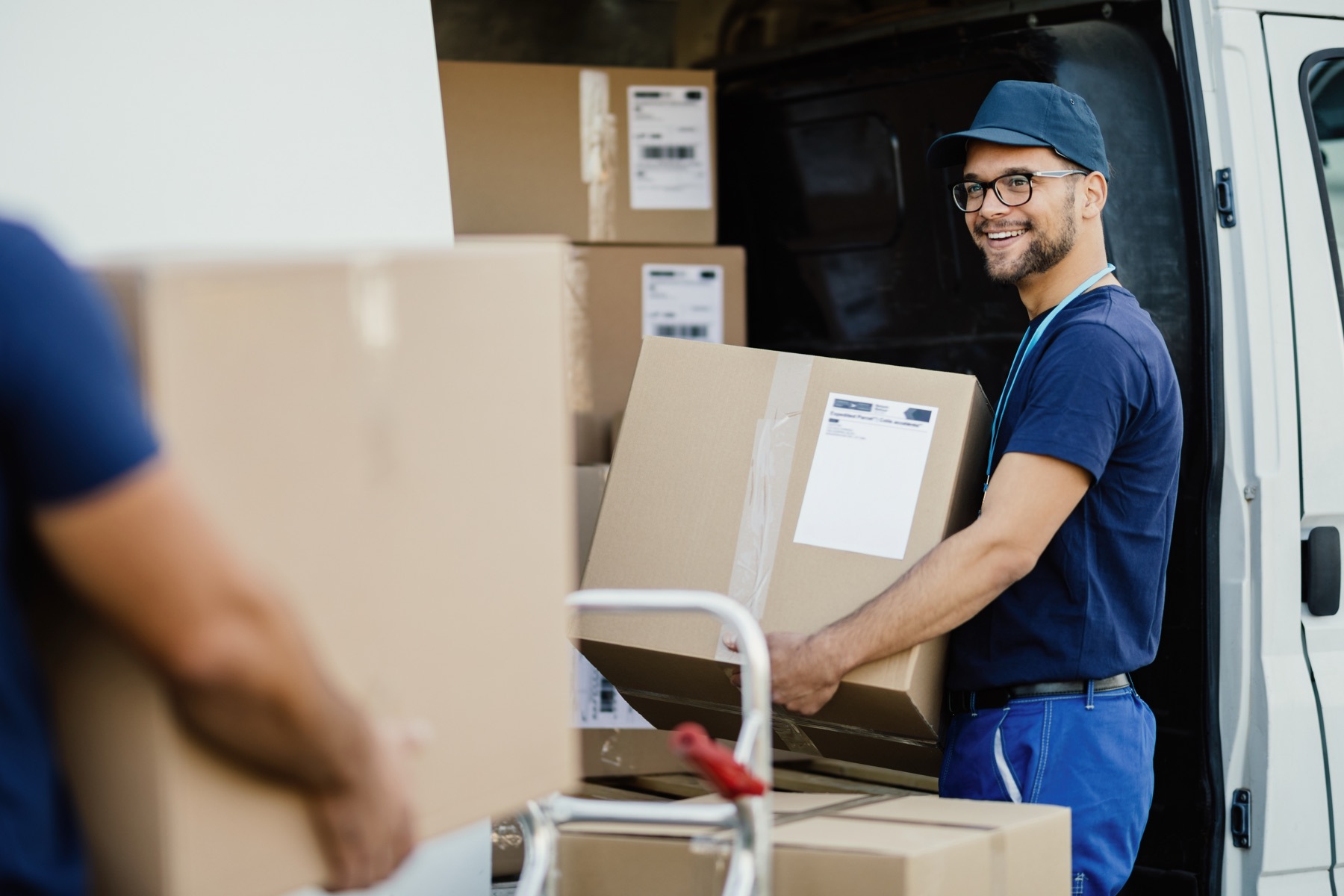 Smiling mover loading boxes into a van with a hand truck